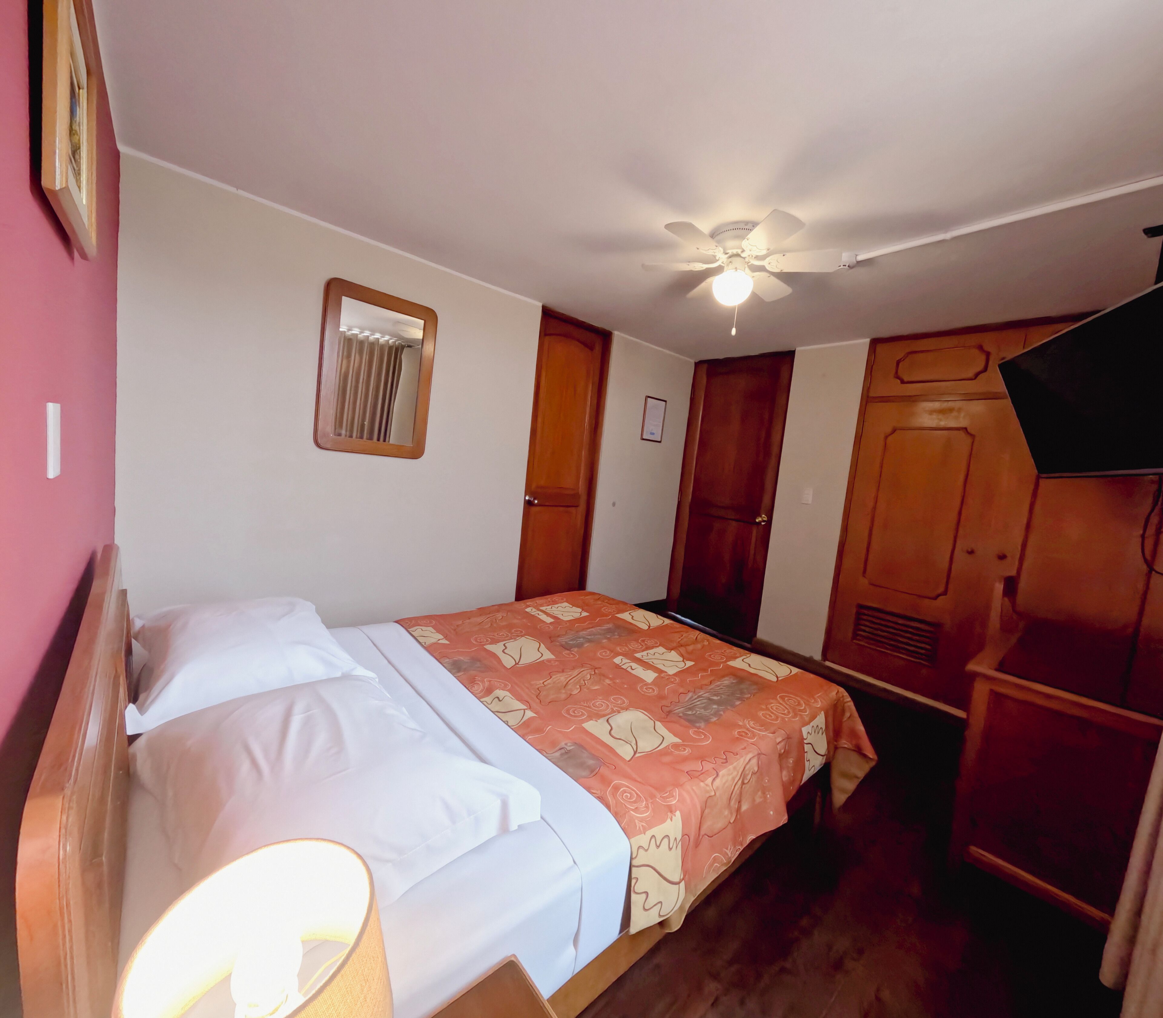 Een slaapkamer met een bed, een plafondventilator, een raam met gordijnen en houten deuren.