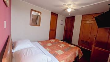 Een slaapkamer met een bed, een plafondventilator, een raam met gordijnen en houten deuren.