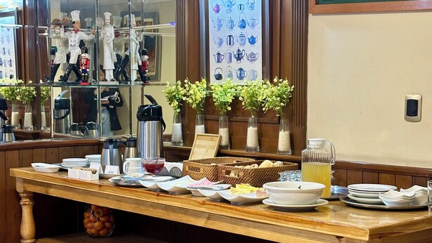 Un buffet de petit-déjeuner proposant une variété de plats et de boissons, une affiche encadrée sur le thème de l’heure du thé et des vases décoratifs.