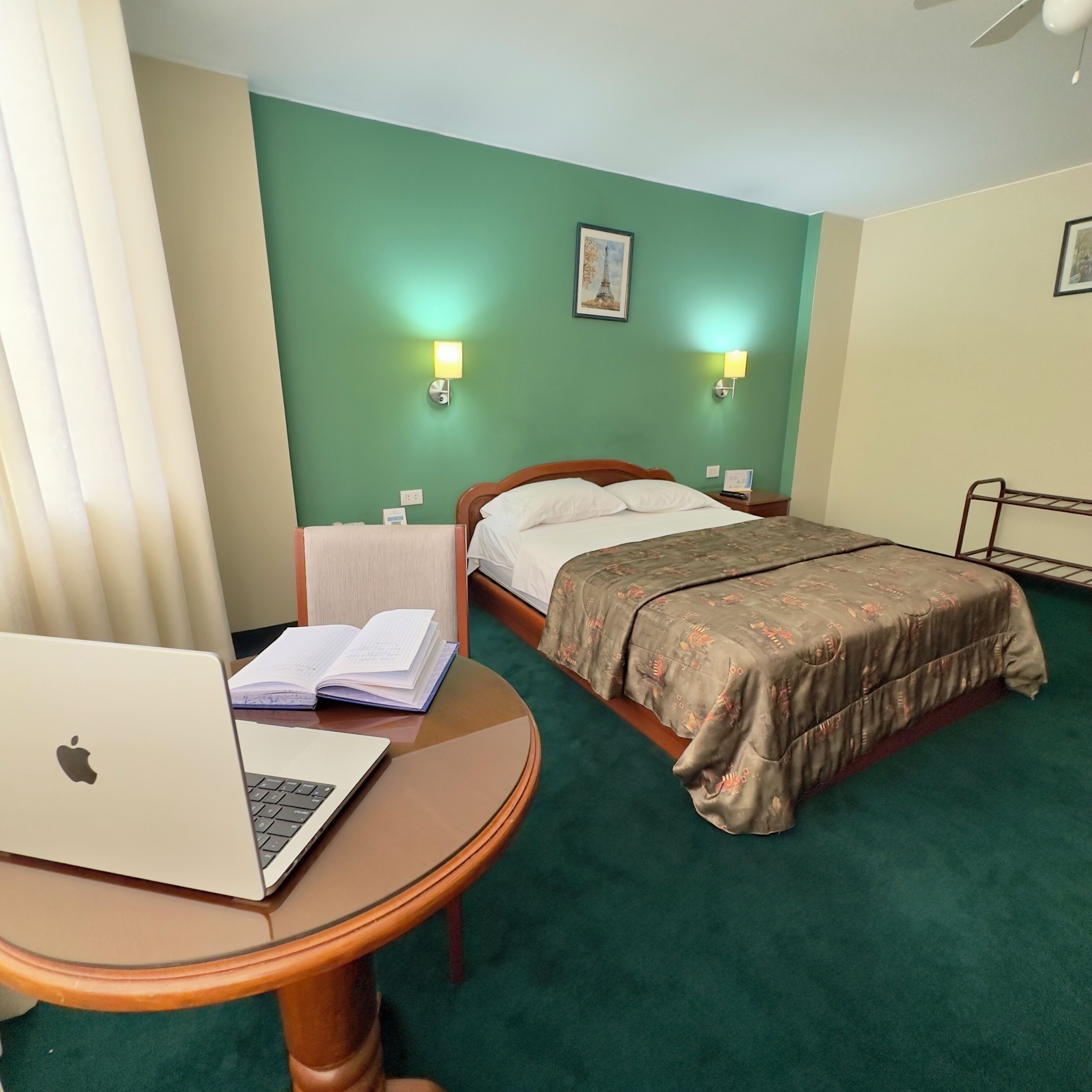 Una habitación de hotel con cama, escritorio con computadora portátil y dos lámparas de pared.