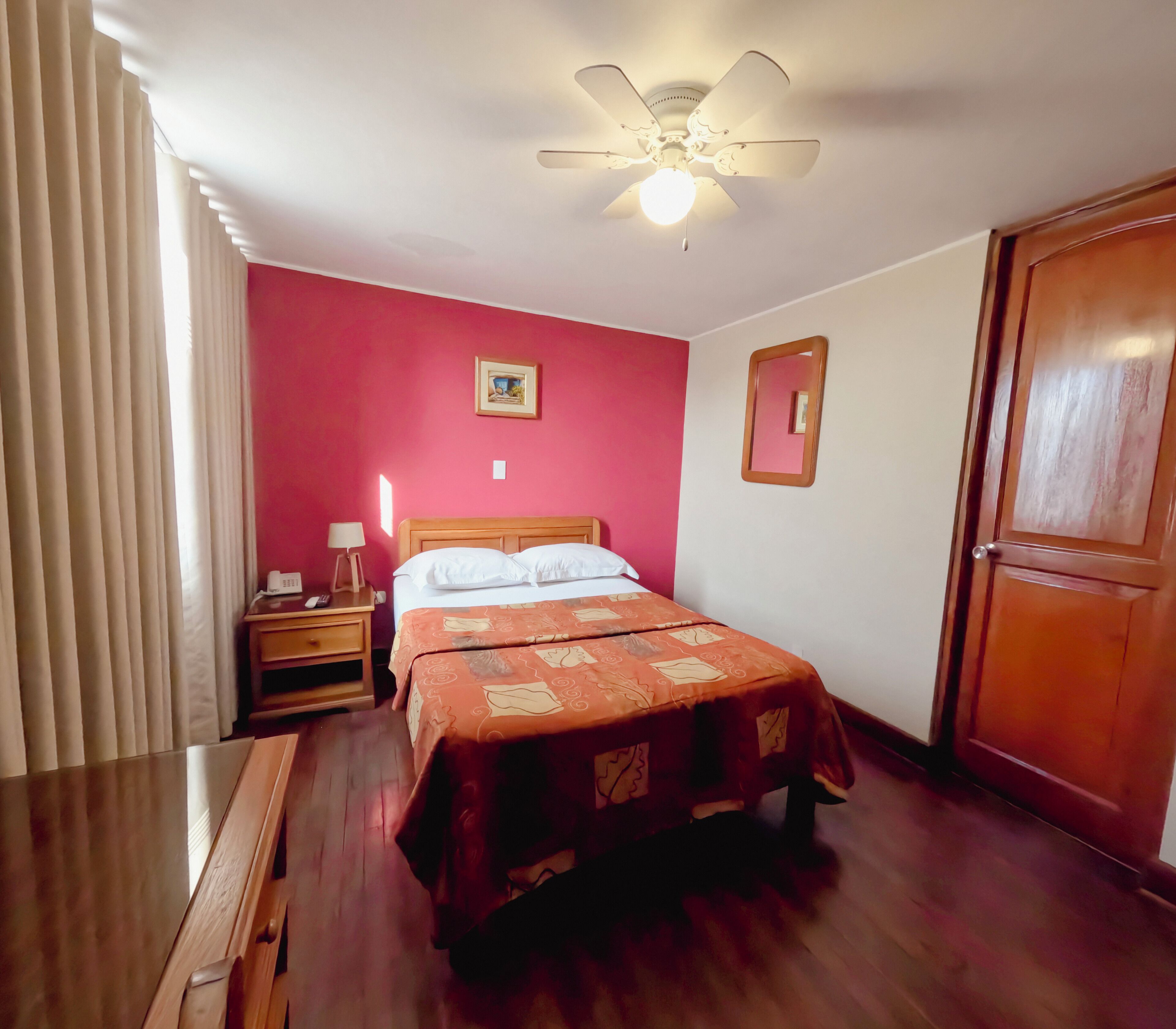 Una habitación de hotel con cama, mesita de noche, lámpara y ventilador de techo.