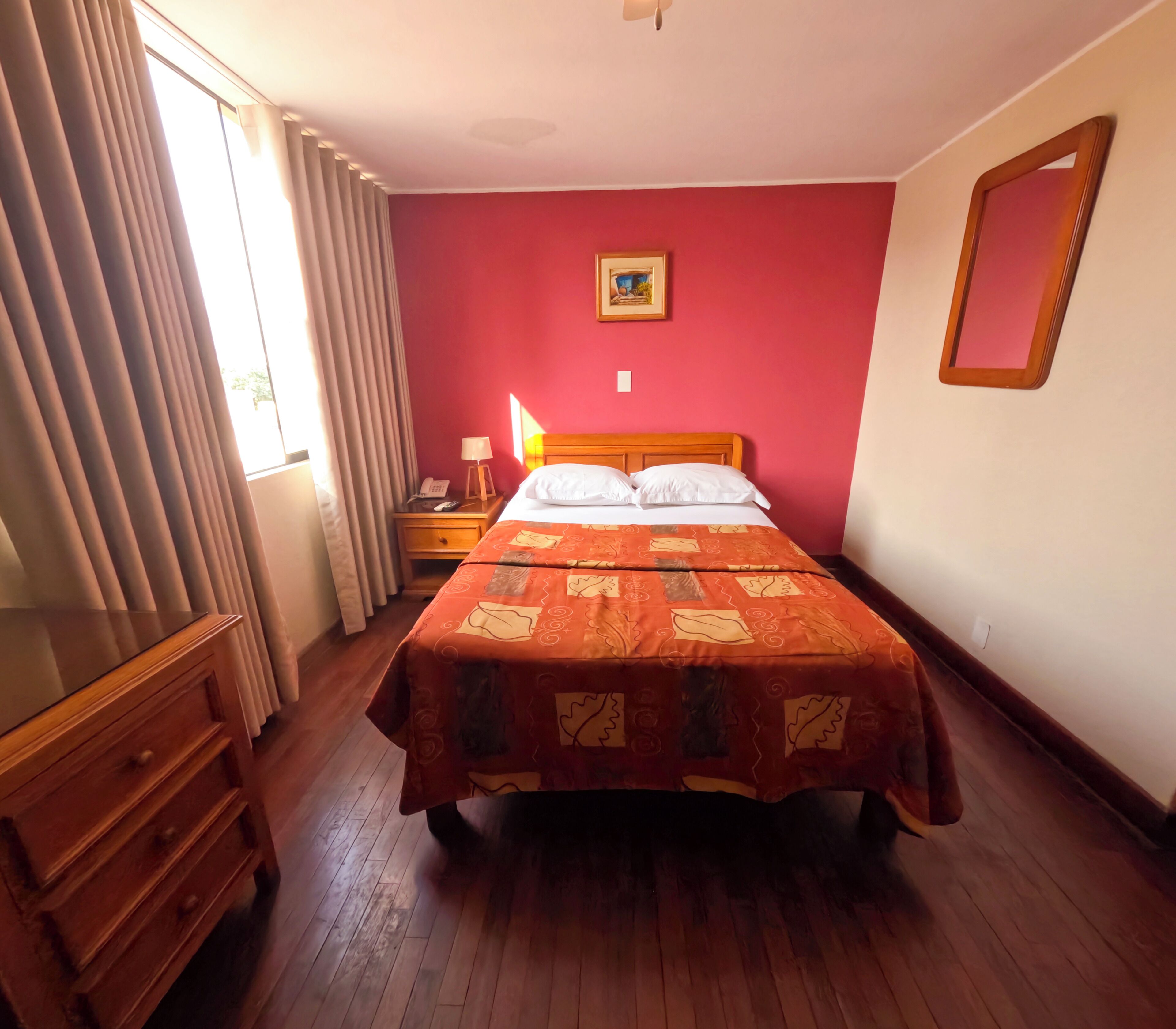 A hotel room with a bed, a bedside table with a lamp, a telephone, and a picture on the wall.