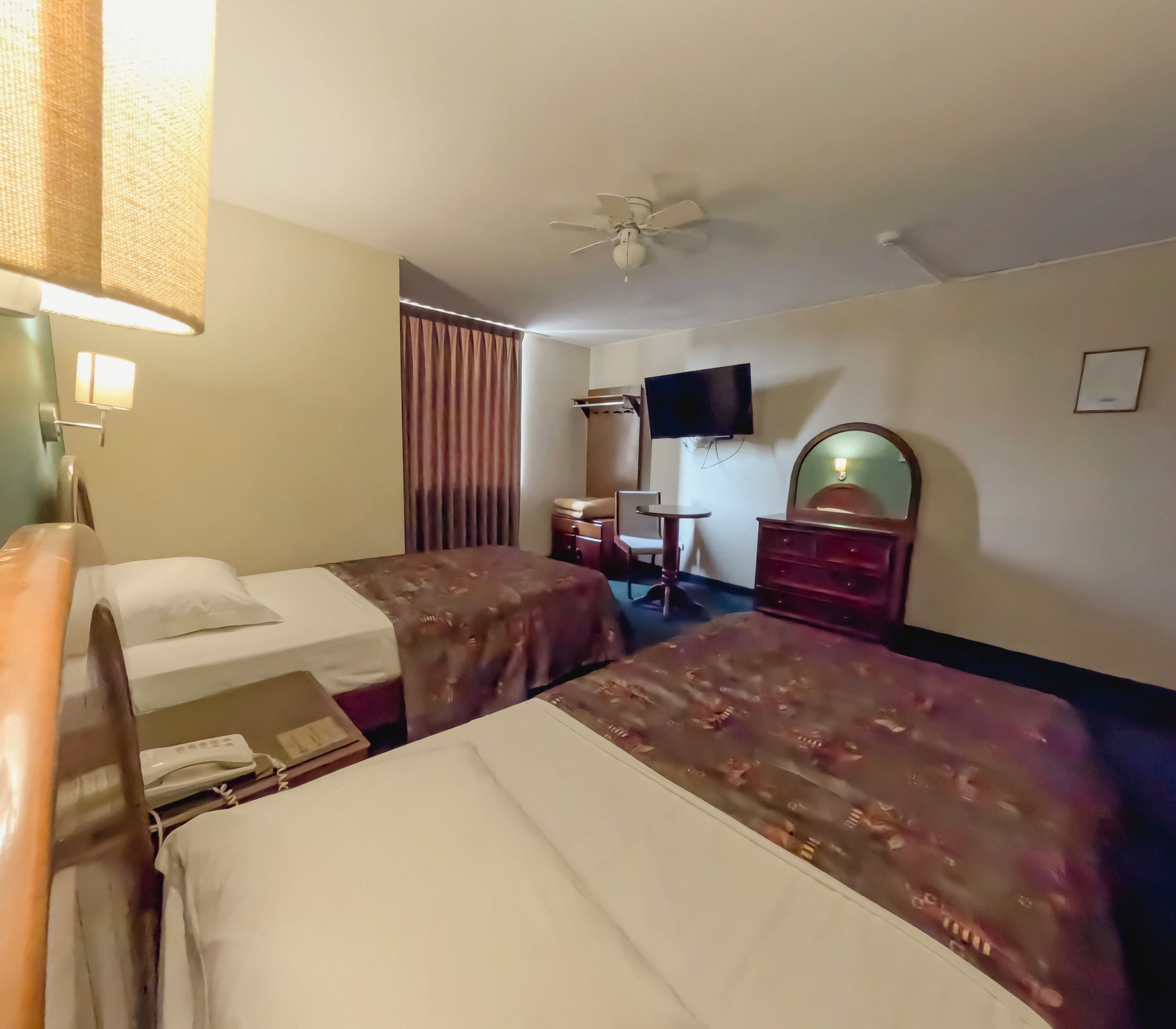 Habitación de hotel con dos camas, un escritorio, una silla, un televisor y un ventilador de techo.