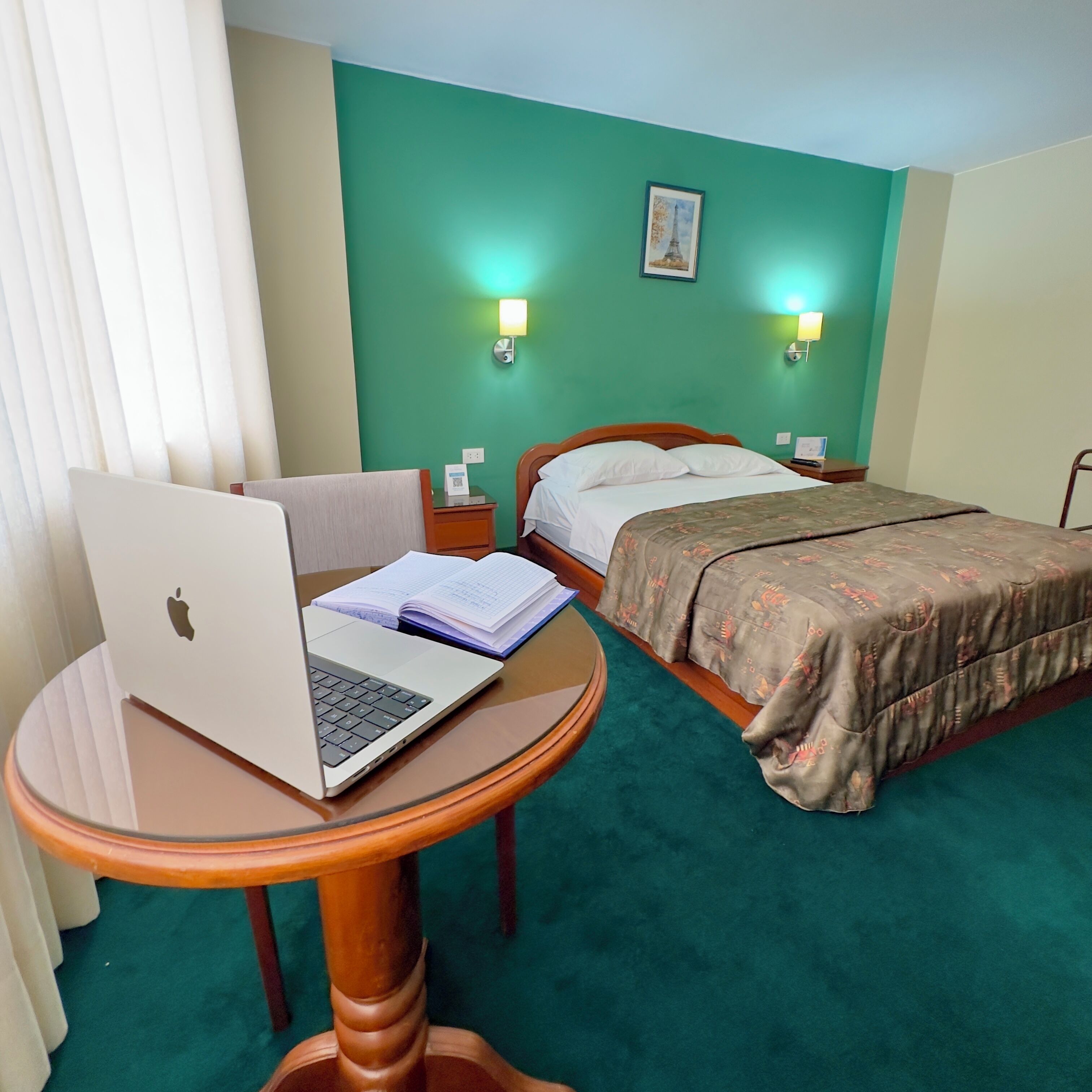 Una habitación de hotel con una cama, un escritorio con una computadora portátil y dos lámparas de noche.