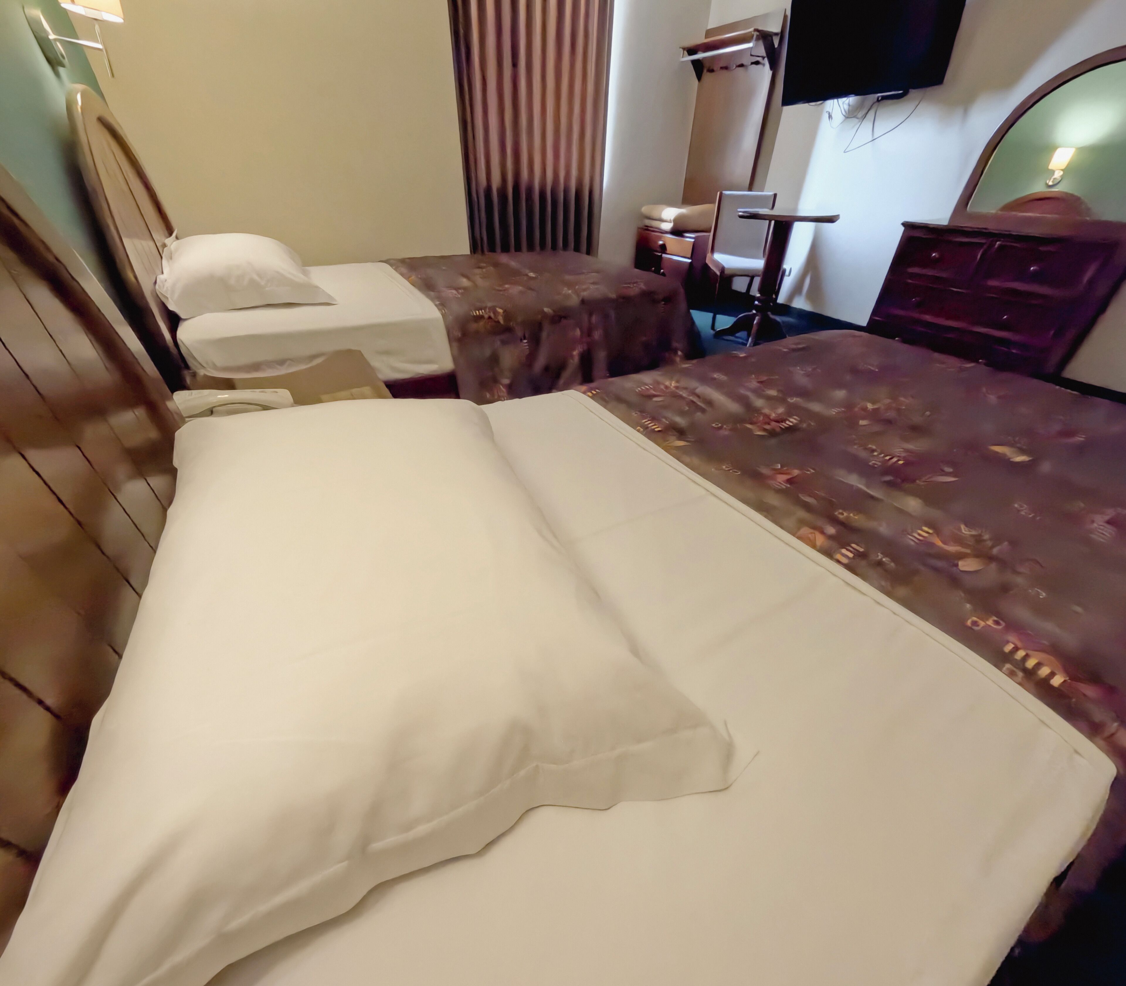 A hotel room with two beds, a television, a mirror, and a dresser.