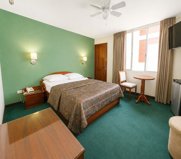 Una habitación de hotel con cama, mesita de noche, silla, pequeña mesa y televisor.