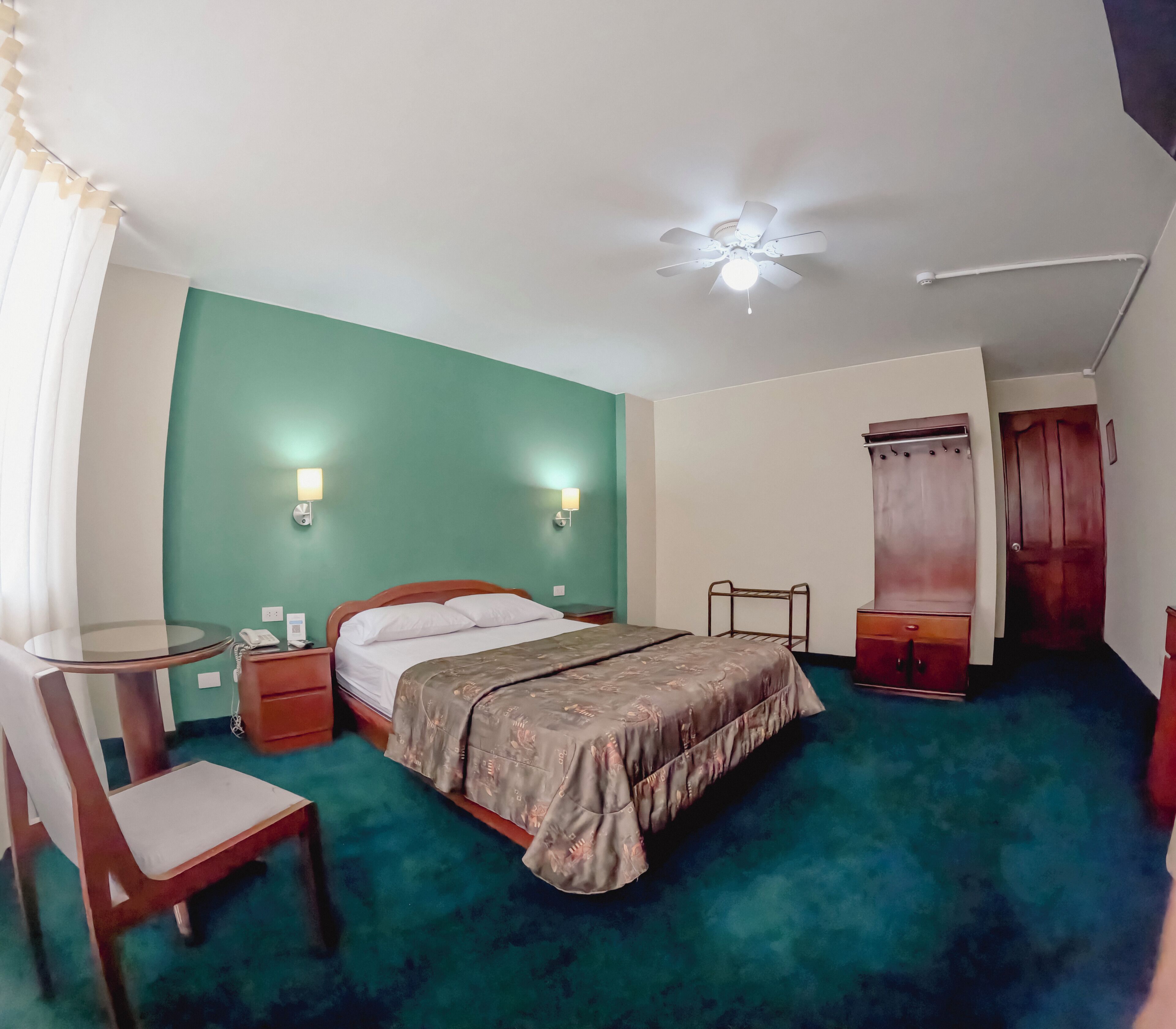A hotel room with a bed, bedside tables, a chair, a wardrobe, and a ceiling fan.