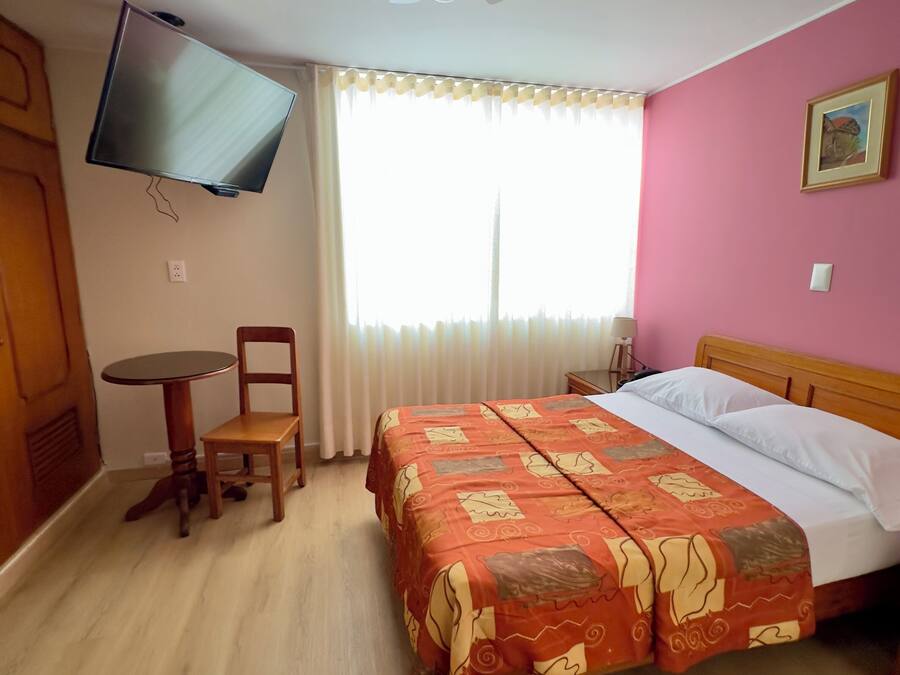 A hotel room with a bed, a desk, a chair, a television mounted on the wall, and a ceiling fan.