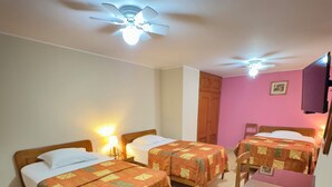 Une chambre d’hôtel avec deux lits simples, une armoire en bois, un bureau avec une chaise et un ventilateur de plafond.
