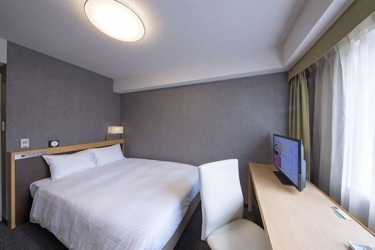 A hotel room with a bed, a desk, a chair, a TV, and a window with curtains.