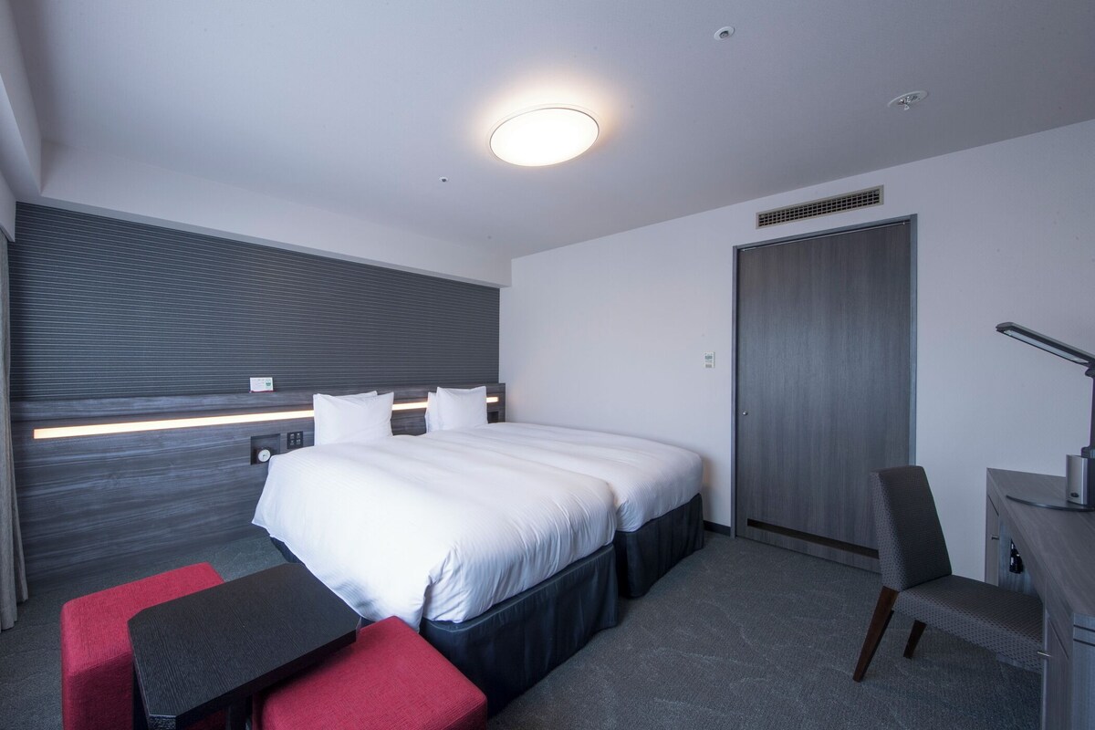 A modern hotel room with a large bed, a desk, and a chair.