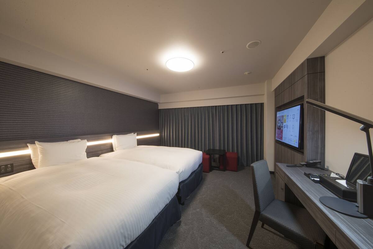 A modern hotel room with a large bed, a desk with a computer, and a TV on the wall.