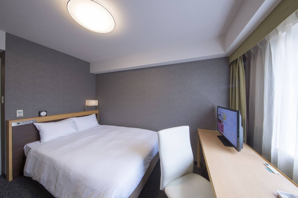 A hotel room with a large bed, a desk with a computer, a chair, and a TV.