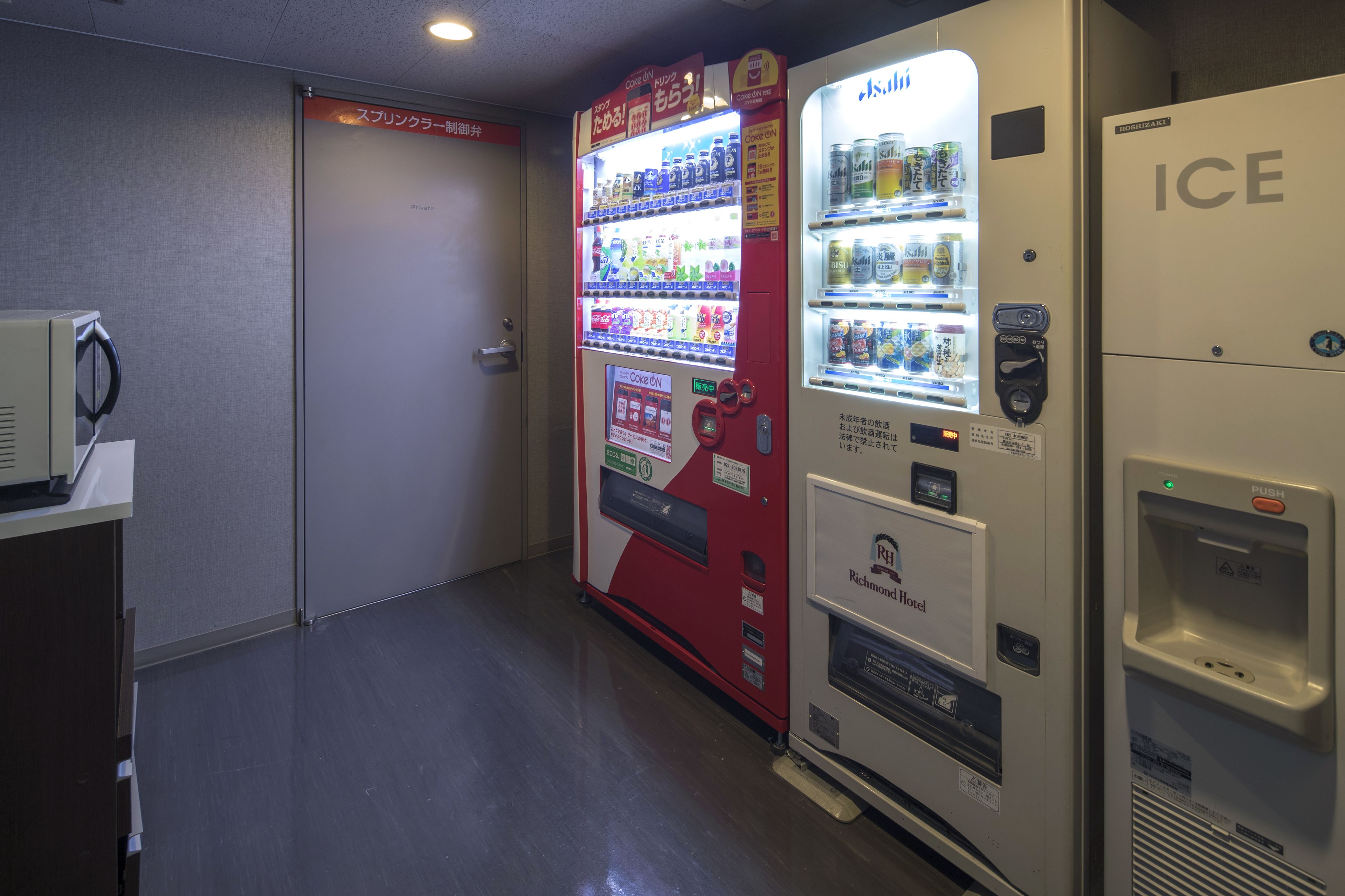 Máquina expendedora con diversas bebidas y aperitivos, un refrigerador con la etiqueta 'ICE' y un cartel anunciando el Richmond Hotel.