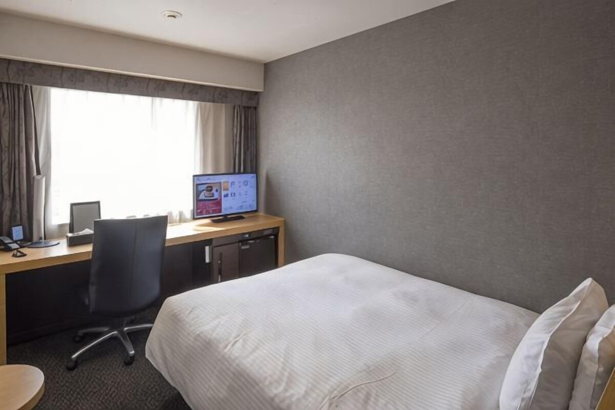 A hotel room with a bed, a desk with a computer, and a window with curtains.