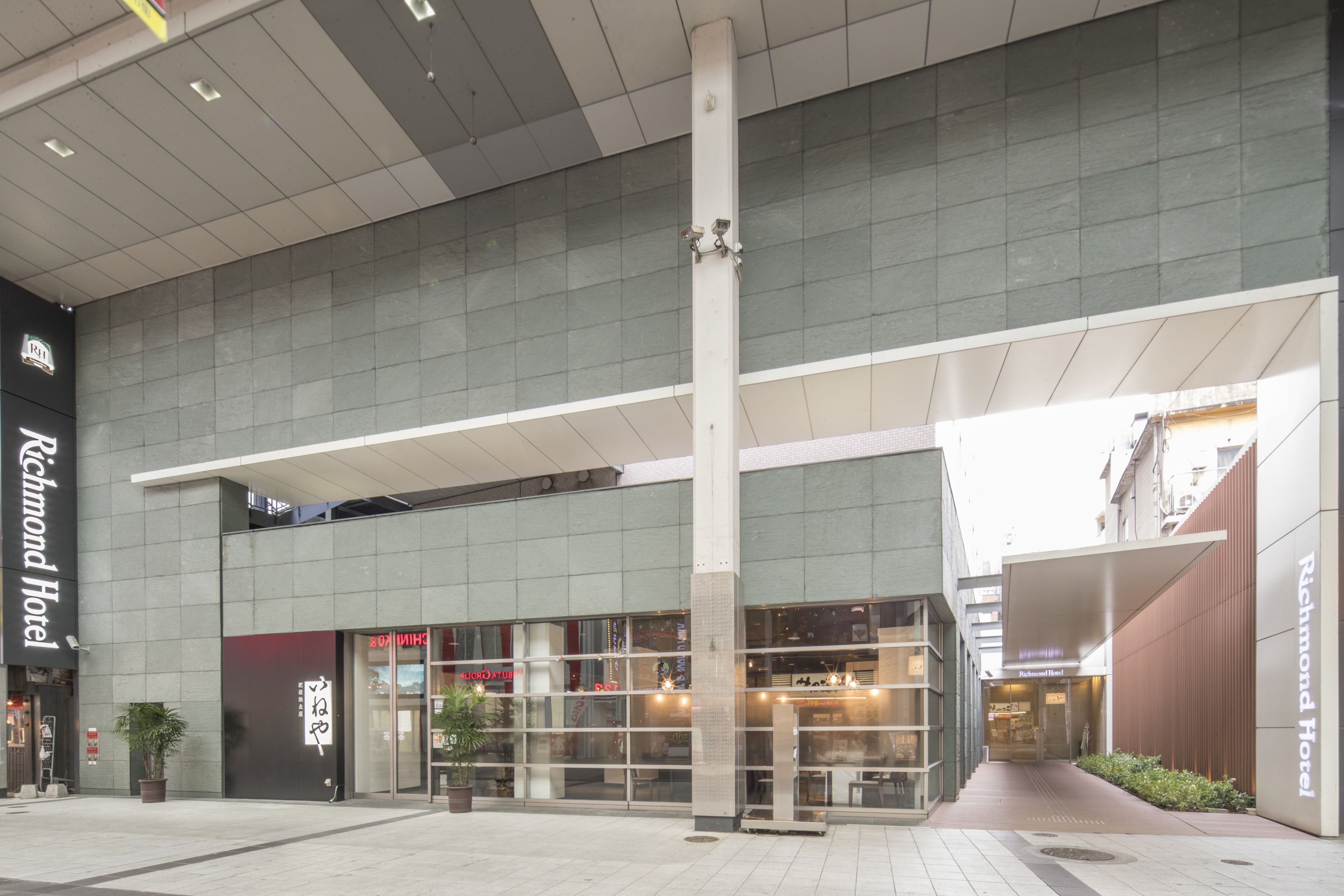 A modern hotel entrance with a glass facade, a prominent vertical column, and a covered walkway.