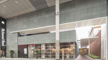 A modern hotel entrance with a glass facade, a prominent vertical column, and a covered walkway.