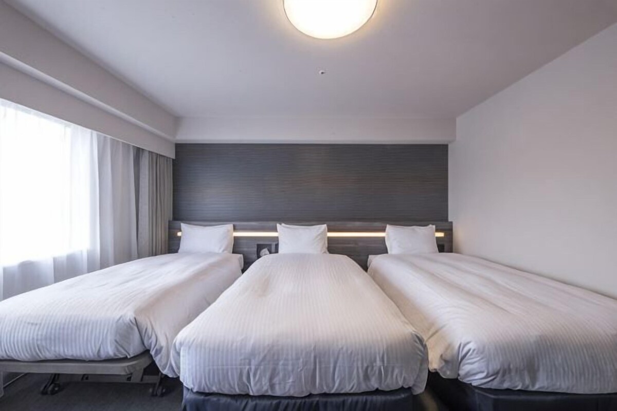 A hotel room with two beds, a large window with curtains, a modern headboard, and a ceiling light.