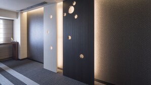 A modern hotel lobby with a reception desk, a large wall with circular cutouts, and a textured wall on the right. - Richmond Hotel Kumamoto Shinshigai (Kumamoto)