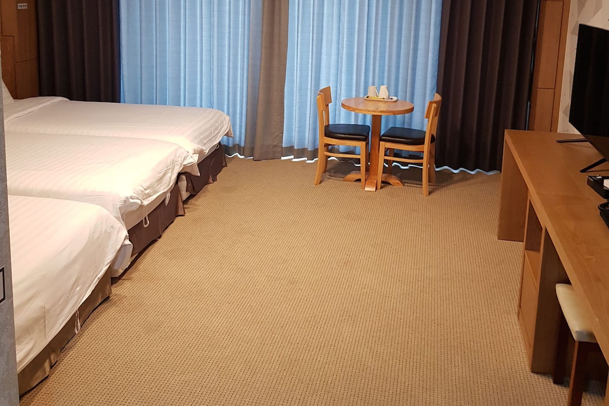 Une chambre d’hôtel avec un grand lit, une petite table ronde avec deux chaises, un bureau et un téléviseur.