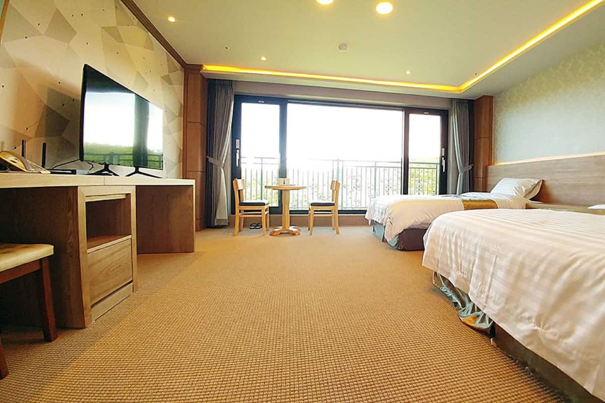 Une chambre d’hôtel équipée d’un bureau, de deux lits, d’une chaise et d’un balcon avec vue.