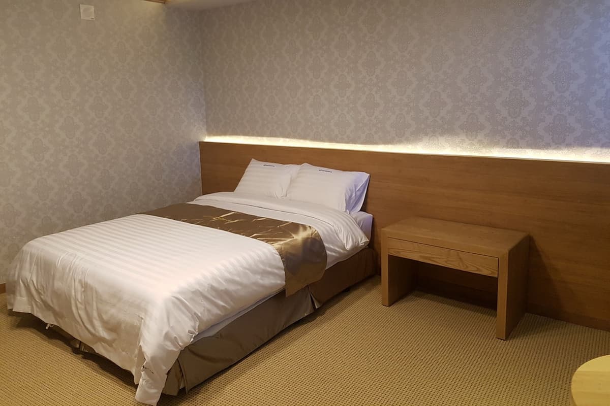 Un lit bien fait, avec une tête de lit en bois, une table de chevet et un mur orné d’un motif.