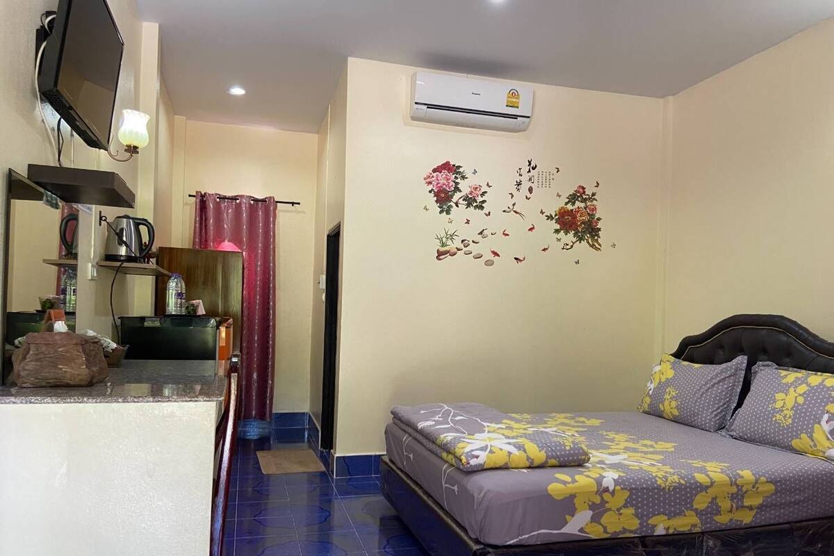 A bedroom with a bed, a TV mounted on the wall, a small kitchenette, and a bathroom with a shower curtain.