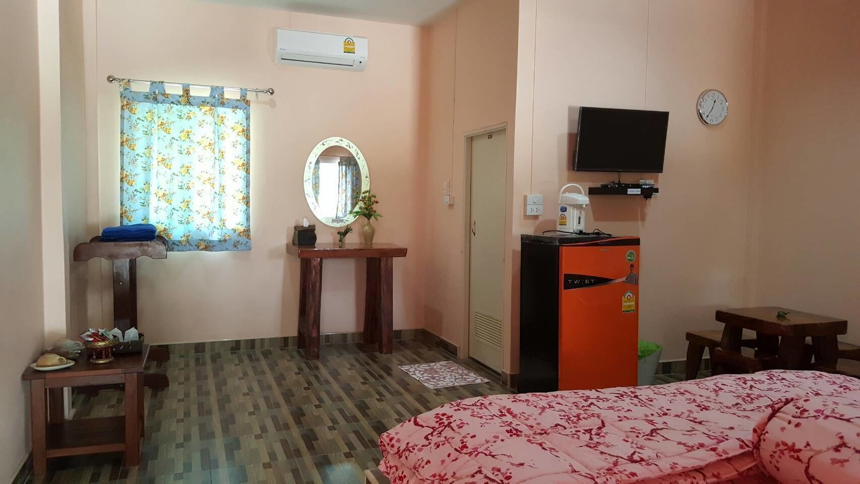 Ein Hotelzimmer mit Bett, Schreibtisch, Fernseher, einer Uhr und einer Minibar.