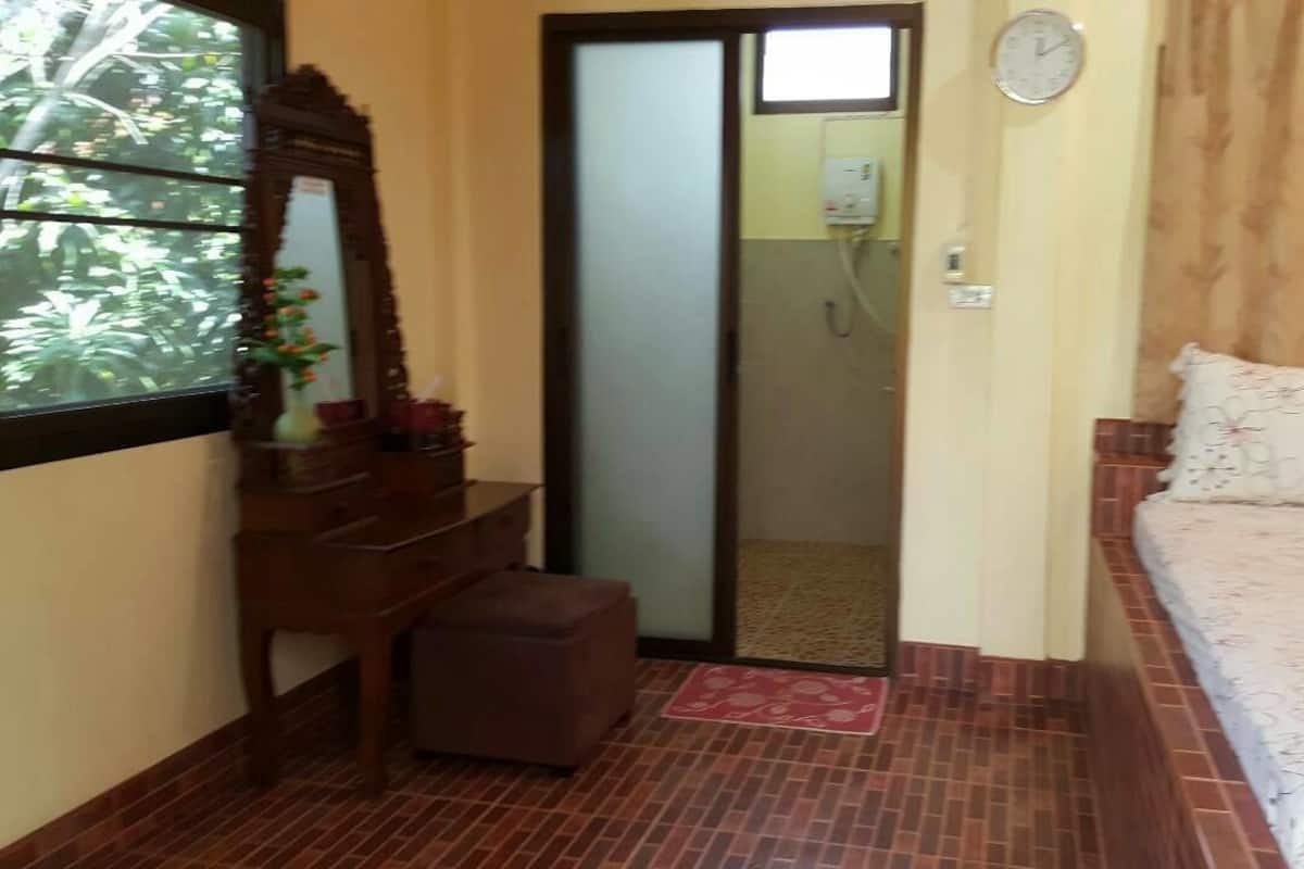 A room with a bed, a wooden dresser, a mirror, and a door leading to a bathroom.