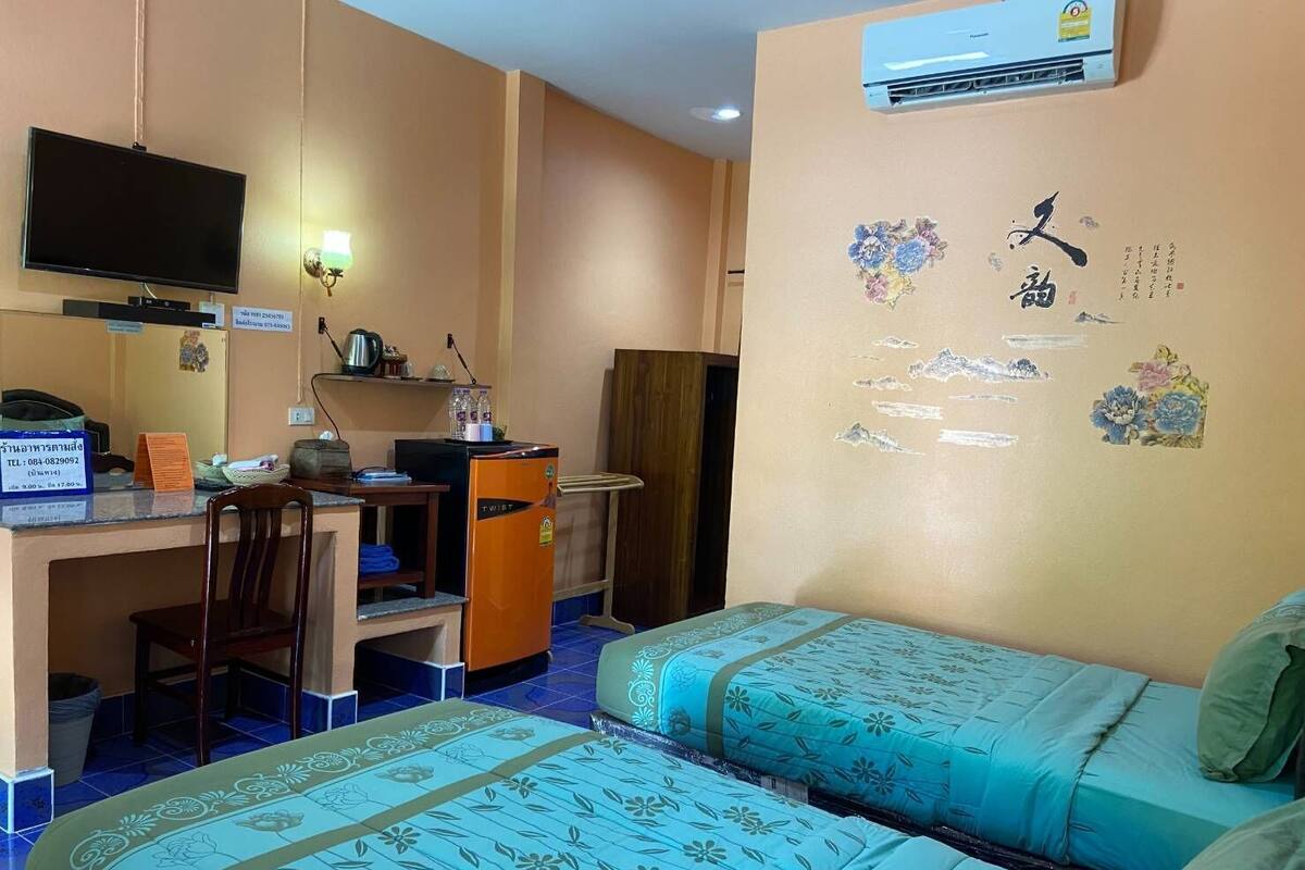 A hotel room with two beds, a desk with a computer, a TV, and a small refrigerator.