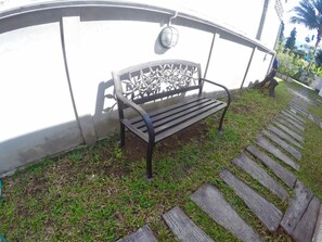 A bench with a metal frame and slatted seat, positioned against a white wall with a decorative metal pattern.
