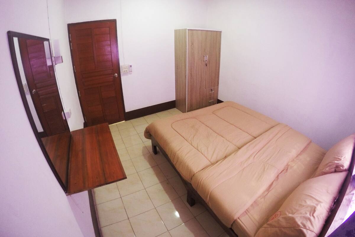 Un dormitorio con cama, un armario de madera, una puerta y una pequeña mesa de madera.