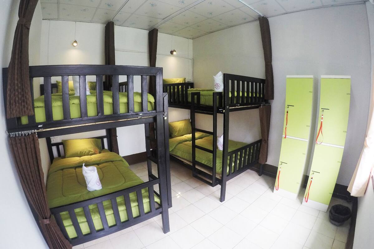 Habitación con literas, ropa de cama verde y suelo de baldosas.
