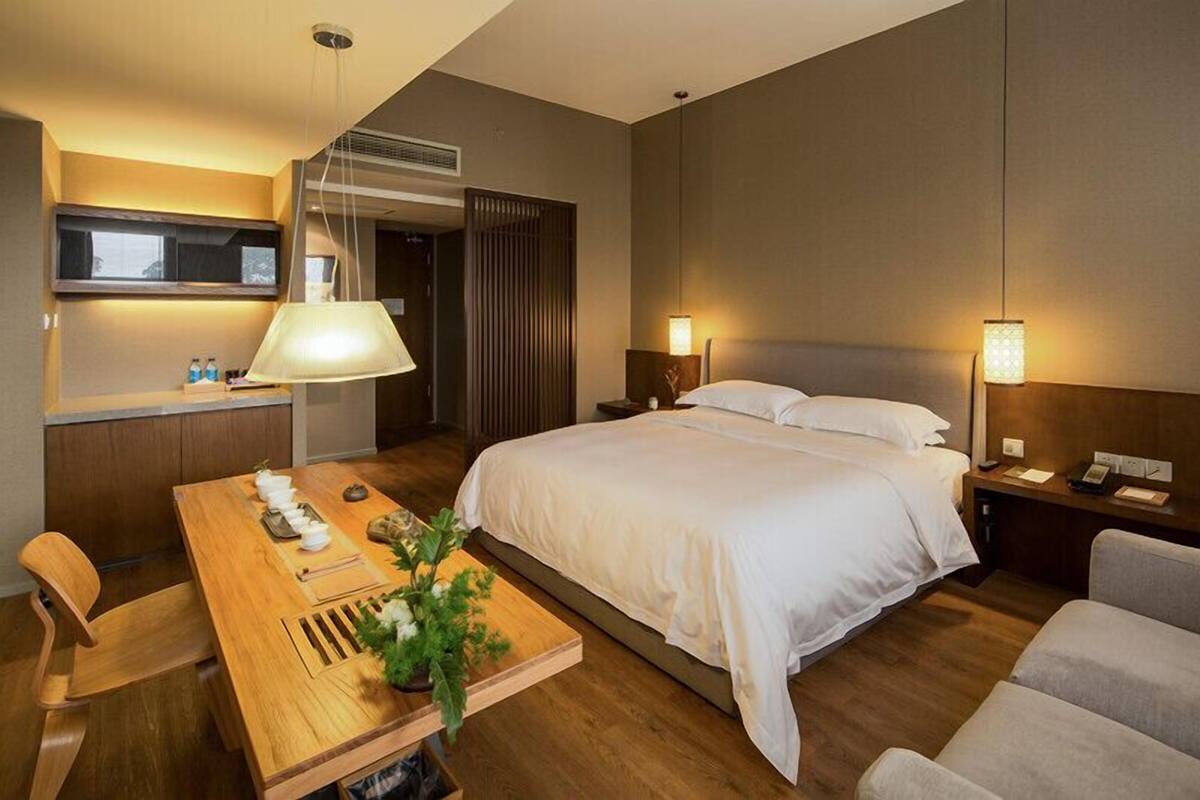 A hotel room with a bed, bedside table, lamp, and a dining area with a table and chairs.
