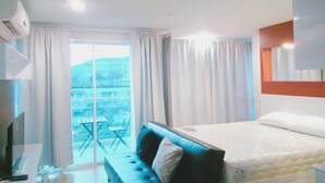Habitación de hotel con cama, televisor, escritorio y balcón con mesa y sillas.