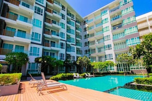 A modern hotel with multiple balconies, a swimming pool, and sun loungers.