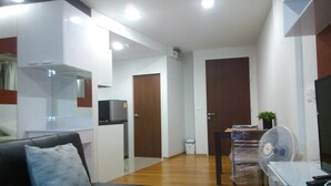 Una sala moderna con un sofá negro, una mesita con una planta, un mueble de televisión blanco y suelo de madera.