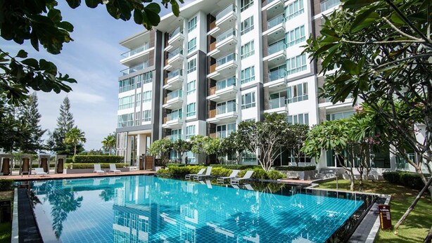 Un hotel moderno con una amplia piscina, rodeado de exuberante vegetación y un edificio de varios pisos con balcones.