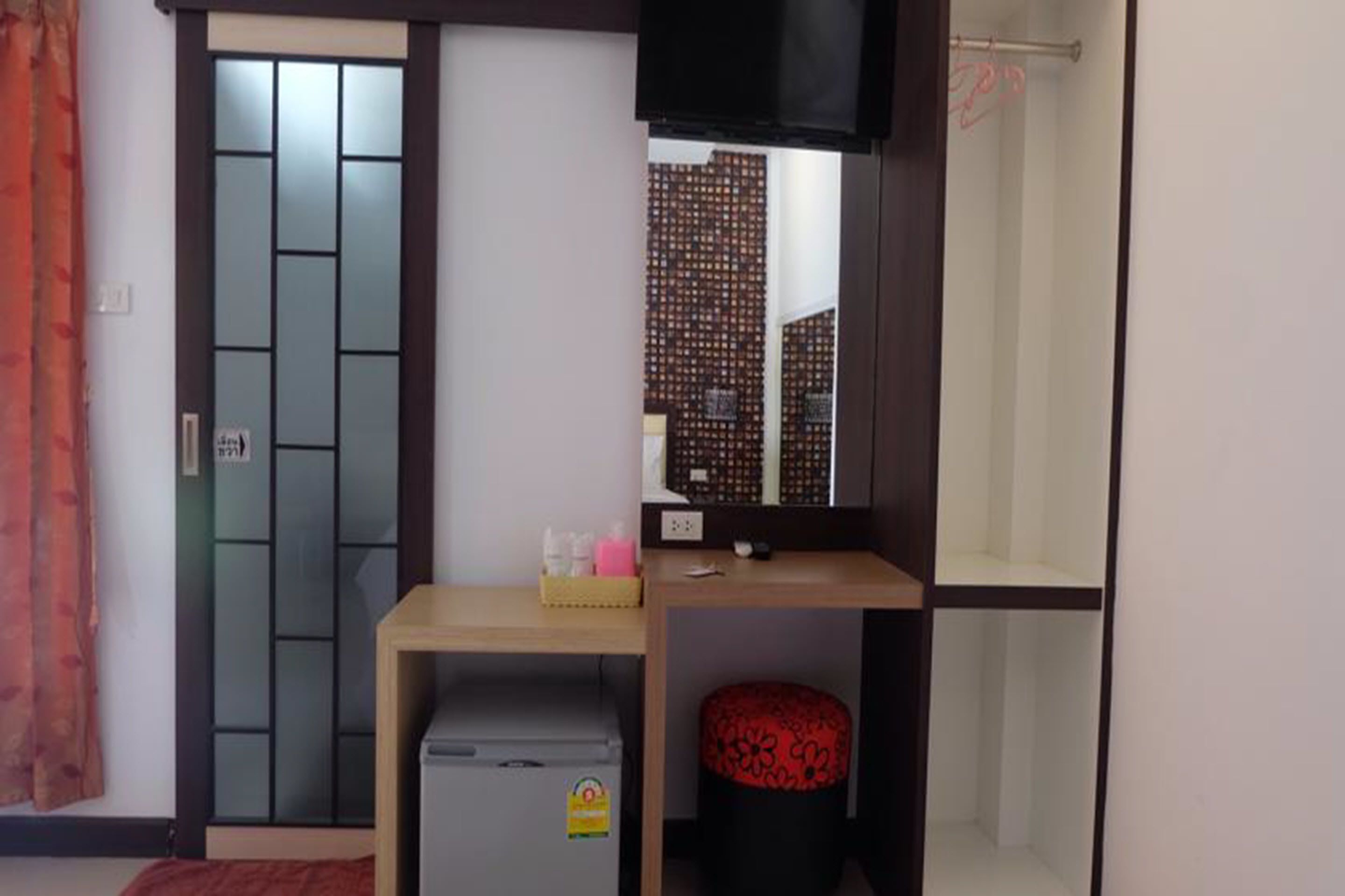 A room with a sliding door, a small desk with a chair, a television, and a red cushioned stool.