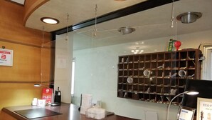 Un mostrador de recepción con separador de vidrio, un letrero de PayPay, una estantería con botellas y un cartel.