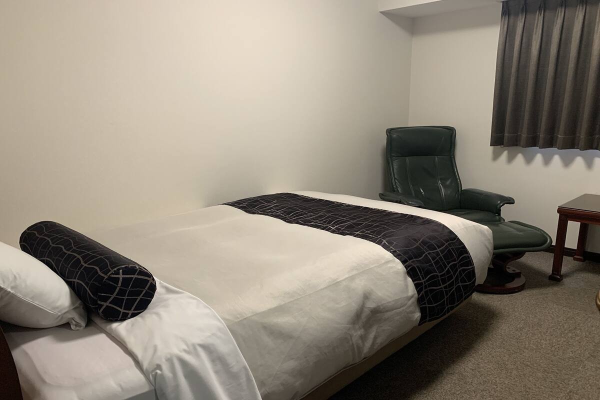 Una habitación de hotel con una cama, una silla verde y una mesita.