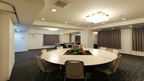 Un salón de conferencias con una mesa redonda, sillas, un centro de mesa floral y un ventanal con cortinas.