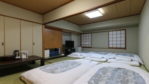 Una habitación de estilo japonés tradicional con suelo de tatami, un futón, un televisor y una pequeña zona de kitchenette.