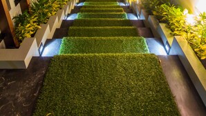 Un escalier moderne avec un revêtement d’herbe artificielle, des rampes en bois et des plantes décorées d’éclairages.