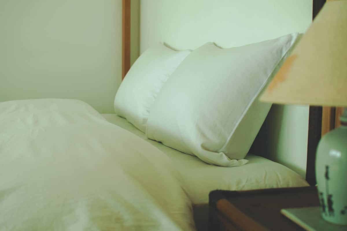 A bed with white bedding and a lamp on a bedside table.