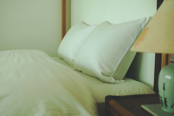 Una cama con ropa blanca y una lámpara en la mesita de noche.