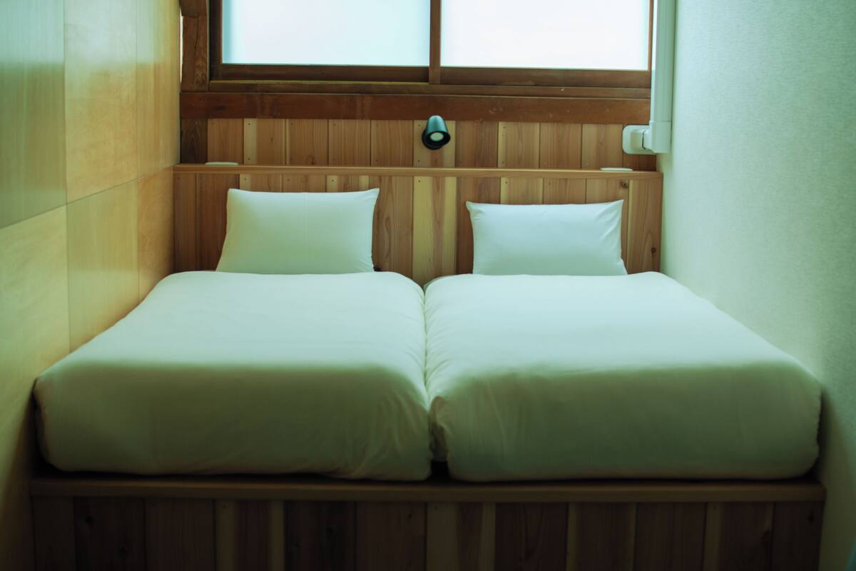 A small, cozy room with two single beds, wooden walls, and a window providing natural light.