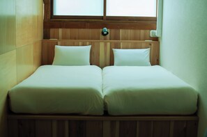 Una habitación pequeña y acogedora con dos camas individuales, paredes de madera y un ventanal que deja entrar luz natural.