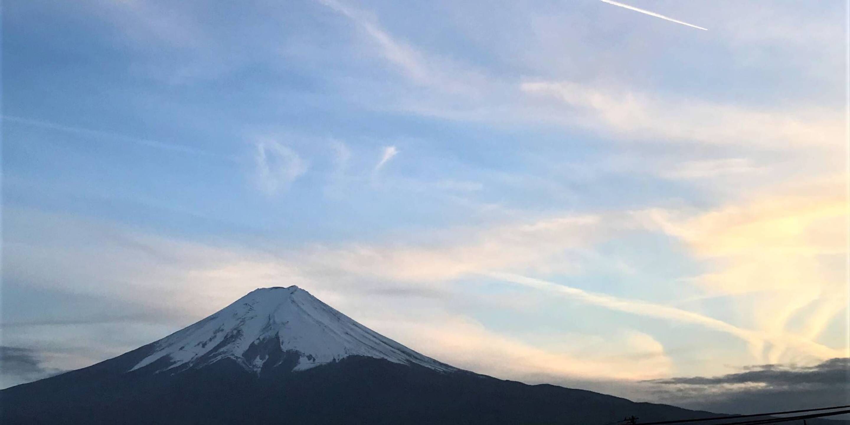 A snow-capped mountain under a clear sky with contrails.
