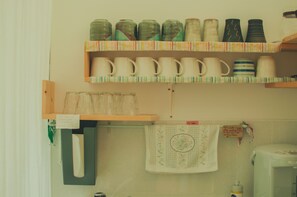 Una cocina con estantes llenos de tazas y recipientes de cerámica, una cafetera y una nota en el perchero.